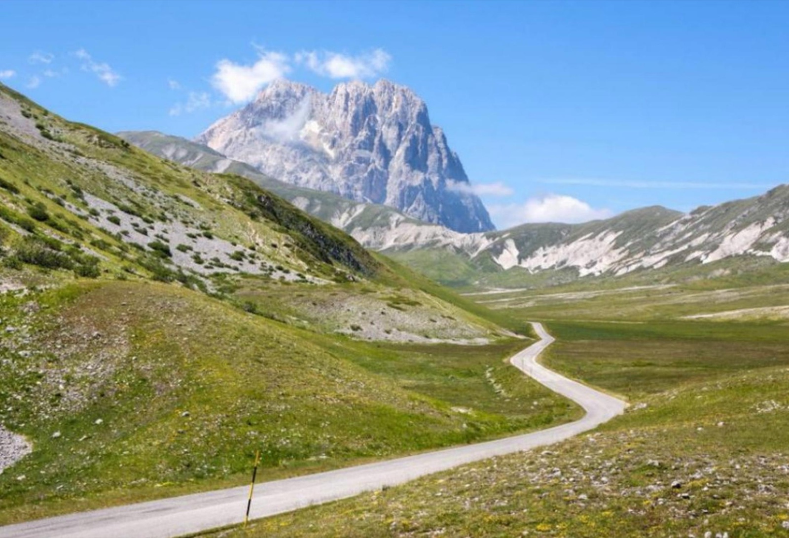 A quiet mountain road winding through high grassland beneath rocky peaks